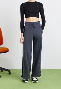 Mörkgrå sweatpants med en avslappnad passform, med dragsko i midjan, vita sidopaneler och en liten logotyp. Parat med en svart crop top.