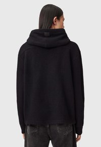 Czarna, textured hoodie z złożonym kapturem i metką z tyłu. Posiada opadające ramiona i luźny krój, zestawione z ciemnymi dżinsami.