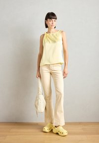 Yellow sleeveless top with a knot detail, cream flared pants, and yellow clogs. The fabric appears soft with a smooth texture.