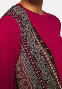 Langärmliges Oberteil in Fuchsia mit gemustertem Seitenbereich, der florale und geometrische Designs in Schwarz, Weiß und Pink zeigt. Weicher Stoff.