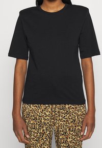 Svart kortärmad t-shirt med rund halsringning och avslappnad passform, i kombination med byxor med leopardmönster, vilket framhäver kontrasterande texturer och färger.