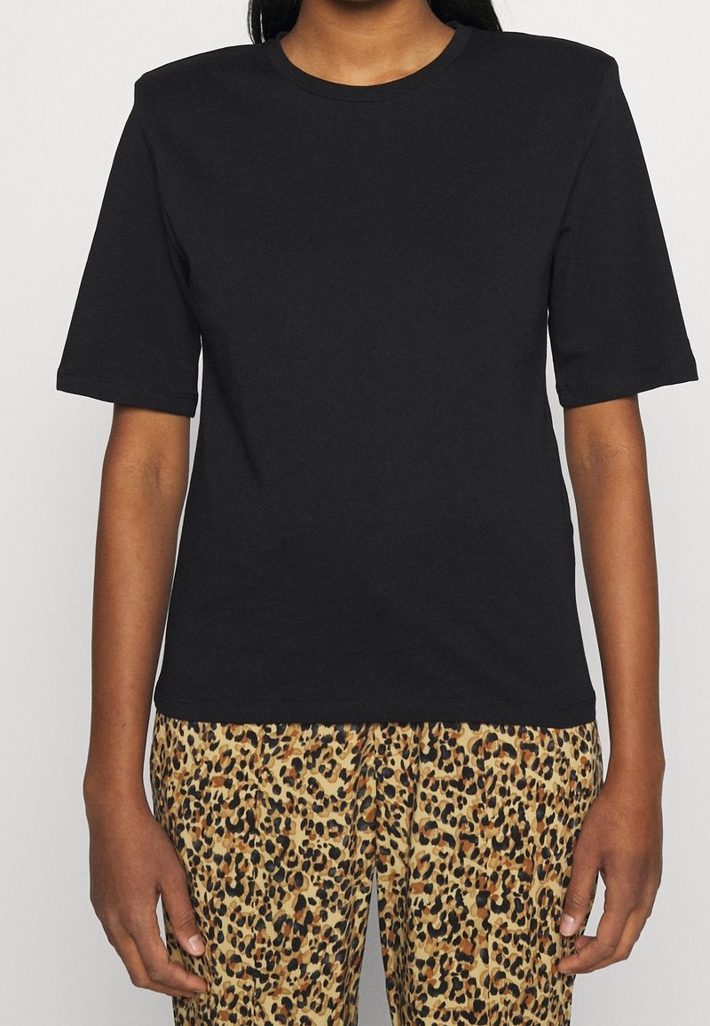 Svart kortärmad t-shirt med rund halsringning och avslappnad passform, i kombination med byxor med leopardmönster, vilket framhäver kontrasterande texturer och färger.