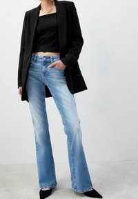Černý blejzr přes černý crop top, v kombinaci se světle modrými zvonovými džíny. Texturované džíny a špičaté černé boty. Viditelné jednoduché doplňky.