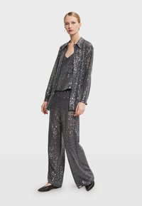 Glinsterende, grijze paillettenoutfit met een losse lange mouwen shirt, tanktop en wijde broek; gladde textuur en reflecterende afwerking.