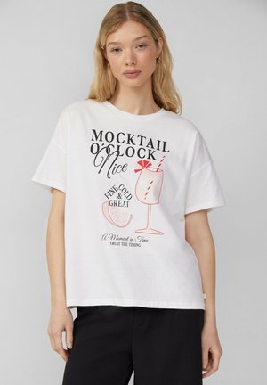 T-shirt en coton blanc avec un imprimé graphique d'un verre à cocktail et un texte en noir et rouge en gras, avec une coupe décontractée et des manches courtes.