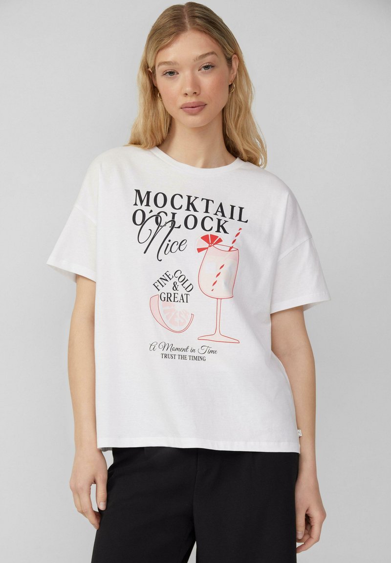 T-shirt en coton blanc avec un imprimé graphique d'un verre à cocktail et un texte en noir et rouge en gras, avec une coupe décontractée et des manches courtes.