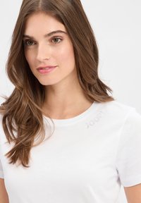 Witte T-shirt met korte mouwen van zachte katoen, met een subtiele accent van rhinestones met de tekst "2021" nabij de schouder.