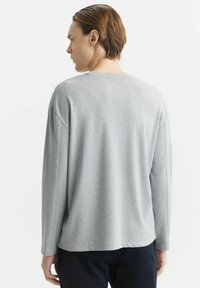 Jasnoszara bluzka z długim rękawem, wykonana z miękkiego materiału, z okrągłym dekoltem i obniżonymi szwami ramion. Projekt jest prosty i casualowy.