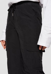 Svarta cargobyxor gjorda av lättviktstyg, med dragsko i midjan, sidofickor och en texturerad yta.