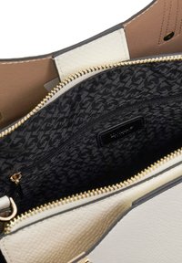 Intérieur de sac à main texturé en blanc avec une doublure à motifs noirs, une poche zippée et des accessoires dorés le long de la fermeture éclair.