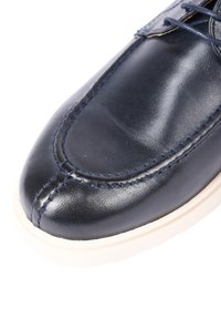 Scarpe in pelle blu navy con texture liscia, punta arrotondata e cuciture a contrasto. La suola in gomma bianca presenta un leggero bordo per una maggiore aderenza.