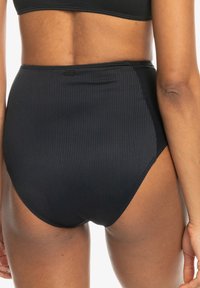 Čierne bikiny s vysokým pásom vyrobené z rebrovanej tkaniny, s hladkým povrchom a jemným značkovým štítkom na zadu.