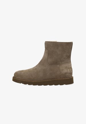 Bruine suède enkelboot met een platte rubberen zool en ronde neus, met zichtbare stiksels en een merkpatch op de hak.