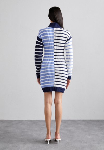 El vestido de punto a rayas presenta un cuello alto, mangas largas y una textura acanalada. Los colores incluyen azul marino, azul claro y blanco en anchos variados.