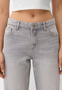 Jean en denim gris à taille haute, avec une légère texture, des poches avant et une fermeture par bouton métallique. Le tissu présente un motif de décoloration subtil.