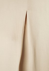 Tissu beige à la texture lisse avec un détail de pli, indiquant une conception sur mesure. Le matériau semble léger et tombe bien.