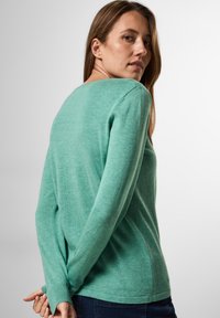 Zelený svetr s dlouhým rukávem vyrobený z měkkého pleteného materiálu, s kulatým výstřihem a žebrovanými manžetami, s volným střihem a hladkou texturou.