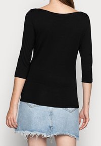 Black, fitted long-sleeve top with a wide neckline and three-quarter sleeves, paired with a frayed hem denim skirt.