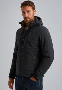 Chaqueta acolchada negra con cierre de cremallera y capucha ajustable. Cuenta con múltiples bolsillos, cremallera en contraste y parche del logo en el hombro.