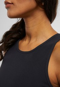 Svart ribbet tanktop med rund utringning, med en tettsittende design og glatt tekstur, vist mot en nøytral bakgrunn.