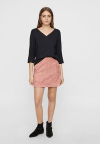 Haut noir à manches longues en v, associé à une mini-jupe en daim rose, avec une texture lisse et une silhouette simple. Bottines noires incluses.