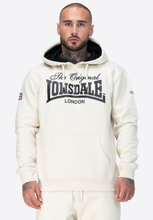 Sudadera color crema con un logo negro que dice "The Original Lonsdale London". Presenta un bolsillo tipo canguro y una capucha con cordón.