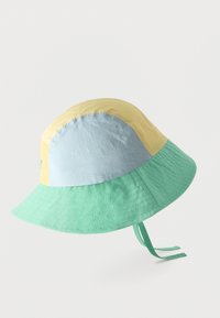 Chapeau seau patchwork pastel avec des panneaux jaune, bleu clair et vert menthe, et des lanières sous le menton sur fond blanc.