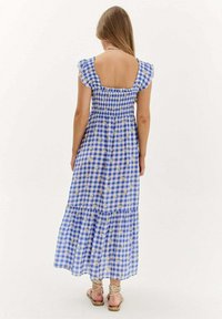 Dlhá modro-biela gingham šaty s volánovými rukávmi, nažehleným telom a vrstvenou sukňou. Obsahuje výrez na chrbte a jemný kvetinový vzor.