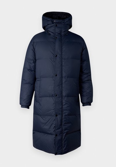 Marineblauwe pufferjas met hoge kraag, drukknoopsluiting en elastische manchetten. Kenmerkt zich door een lange, geïsoleerde pasvorm met een gladde textuur.