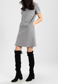 Grå klänning med kort ärm och avslappnad passform, med sidofickor. Kombinerad med höga svarta mockastövlar som visar en slapp textur.