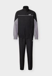 Μαύρη και γκρι φόρμα με ζακέτα με φερμουάρ που διαθέτει ψηλό γιακά, ελαστικά μανίκια και ταιριαστό παντελόνι. Το υλικό έχει ομαλή υφή.