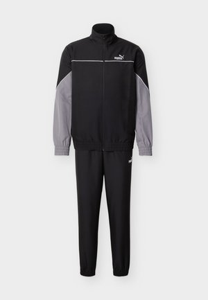 Juodas ir pilkas sportinis kostiumas su užtraukiama striuke, kurioje yra aukšta apykaklė, elastinės rankogaliai ir derančios kelnės. Medžiaga turi lygią tekstūrą.