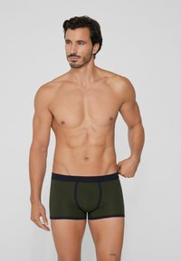 Dunkelgrüne Boxershorts mit einem marineblauen Bund, ausgestattet mit einem Frontpouch, glatter Textur und kurzem Beinansatz.