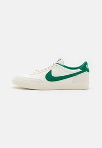Valge nahast spordijalats, millel on roheline sametist Swooshi logo ja kanna aktsendid. Omab ümarat varbaosa ja tekstuurset kummist tallat, klassikaline lace-up disain.