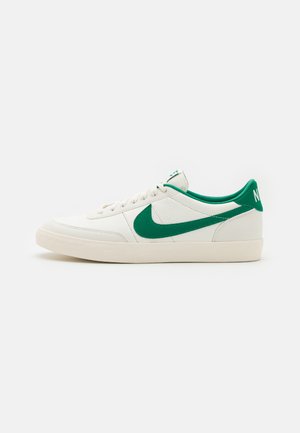 Hvit lær sneakers med grønn mocka Swoosh-logo og hælakkenter. Har en rund tå og strukturert gummisåle, klassisk snøring.