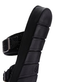 Zwarte sandaal met een gestructureerde bovenkant, rhinestone accenten, verstelbare gesp en een dikke, groefde rubberen zool voor grip.