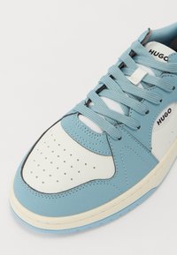 Sneaker in pelle blu chiaro con accenti bianchi, punta perforata, lacci spessi e cuciture nere. Logo del marchio "HUGO" visibile sul lato.