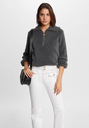 Sudadera de forro polar gris con media cremallera, que presenta una textura suave y puños enrollados. Combinada con pantalones blancos de talle alto y un bolso negro bandolera.