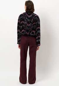 Zwarte cropped trui met kleurrijke pailletten golfpatronen, gecombineerd met hoog-getailleerde bordeauxrode wijde broekspijpen. Glad textuur overal.