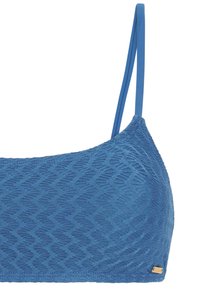 Sininen teksturoitu bralette, jossa on ohuet kaksinkertaiset olkaimet ja pieni kultainen suorakaiteen muotoinen tunniste oikeassa alareunassa.