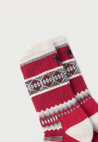 Neulotut punaiset sukat, joissa on kermaisen värinen varsi ja harmaan, mustan ja punaisen geometrinen kuvio. Pehmeä tuntuma, polven keskikorkeus ja vahvistettu kantapää.
