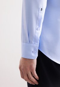 Hand van een man rustend naast de lichtblauwe dress shirt manchet met knoop en kleine zwarte rozenborduursel op de mouwplacket.