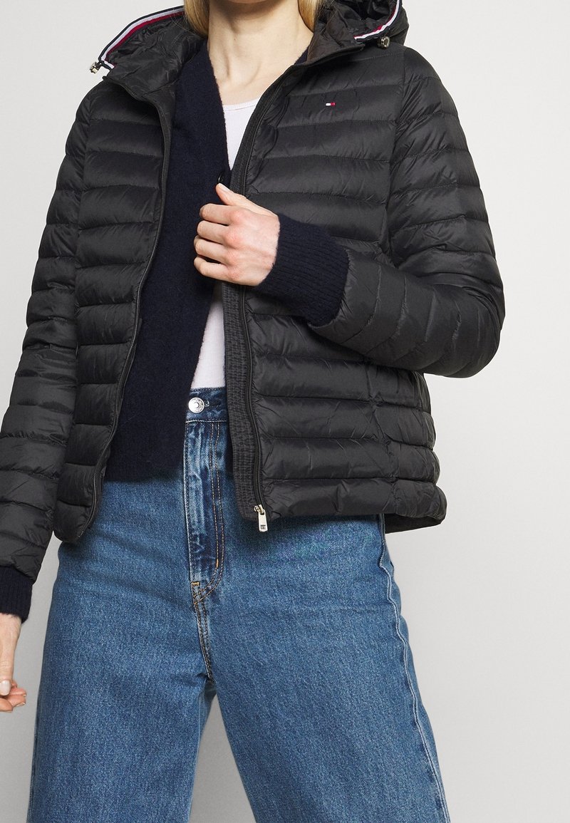 Giubbotto imbottito nero con design trapuntato, chiusura con zip e cappuccio regolabile; presenta polsini a coste e una fodera interna con accenti di colore a contrasto.