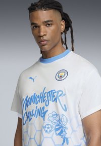 Tricou alb din bumbac, cu accente albastre, guler tip crew, grafică "Manchester Calling" și logo-ul Manchester City pe piept.