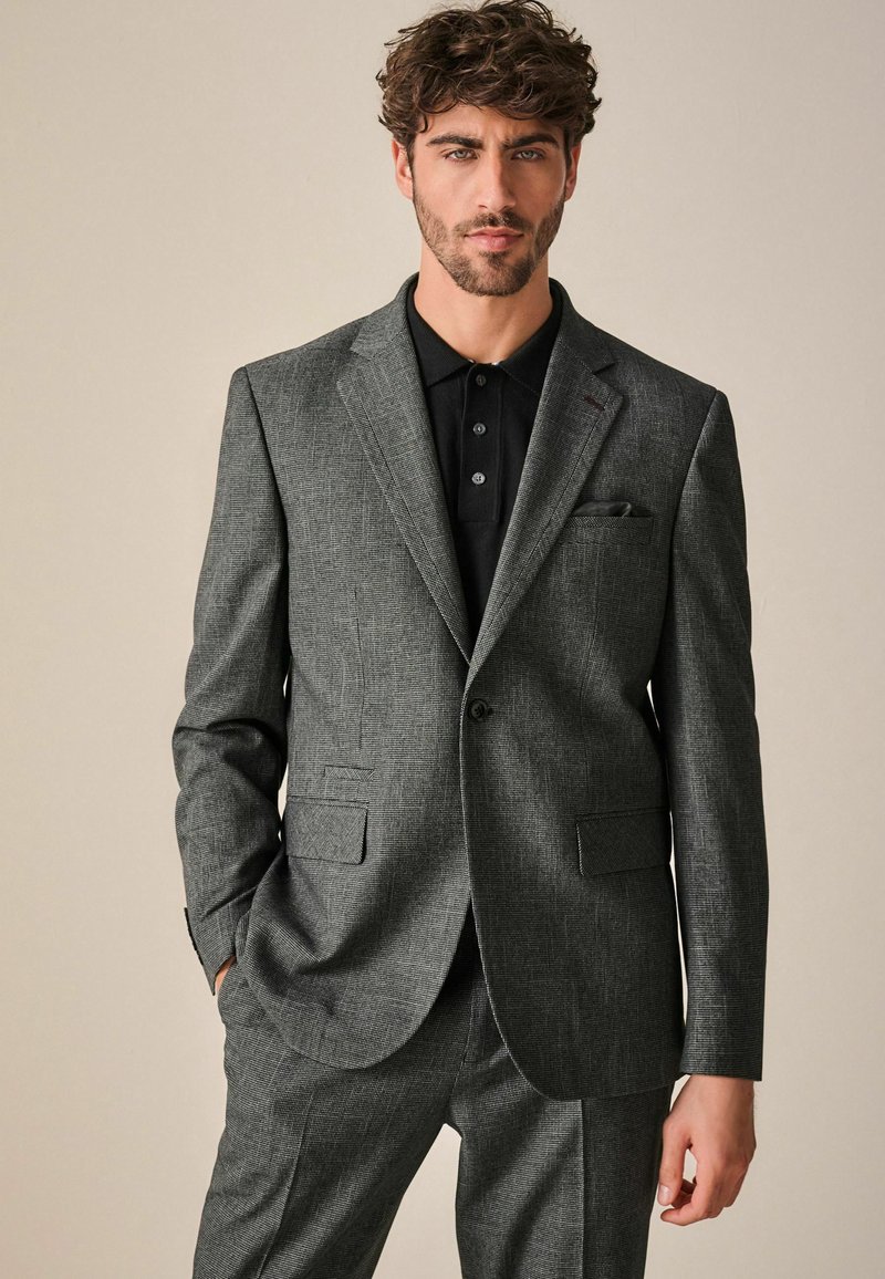 Dunkelgraue strukturierte Anzugjacke mit Reverskragen und zwei Fronttaschen, getragen über einem schwarzen Poloshirt. Slim Fit Design.
