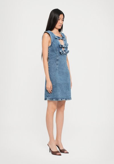 Denim-mekko, jossa on tiukka siluetti, syvä V-aukko ja röyhelökoristeet kaula-aukossa, vaaleansininen ja hienovaraisella tekstuurilla.