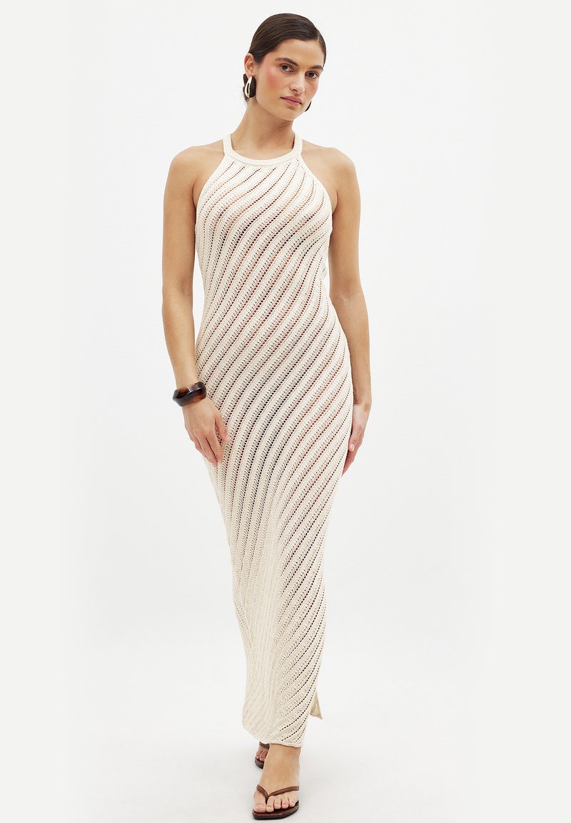 Maxi dress in tessuto a maglia crema, con un motivo a onde, design senza maniche e fessure laterali. Abbinata a un bracciale marrone e sandali.