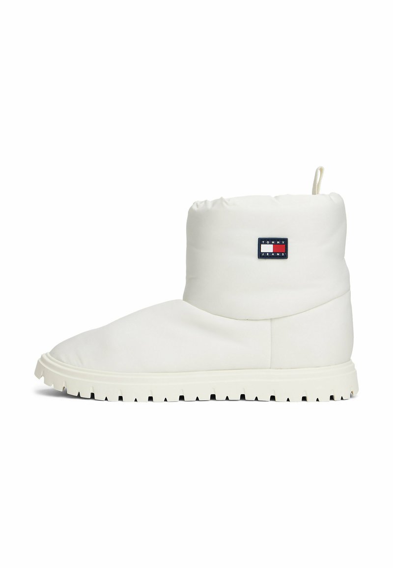Botín acolchado blanco con punta redonda, suela de goma texturizada y un pequeño parche de logo en azul marino, rojo y blanco en el costado.