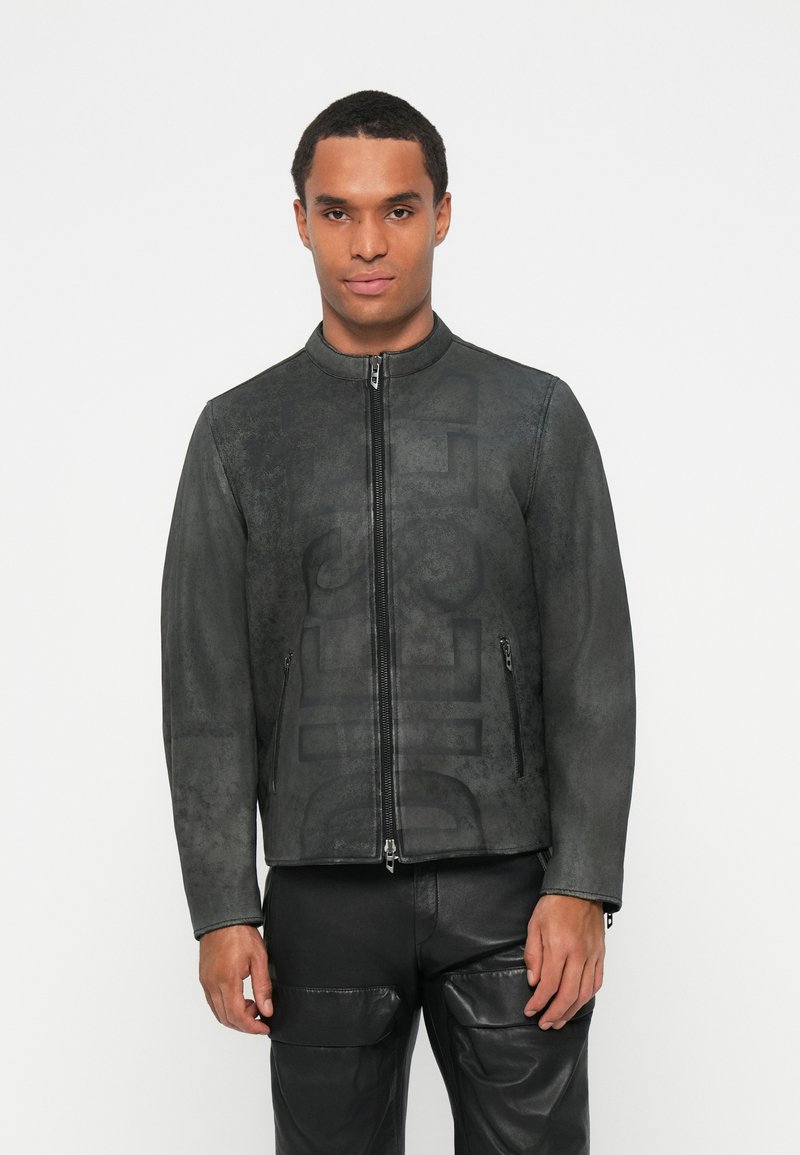 Chaqueta de cuero sintético negra con un alto cuello, cremallera frontal y bolsillos laterales. Presenta un sutil patrón grabado en la tela.