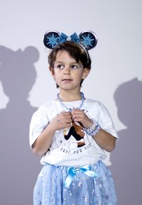 Bambina che indossa una maglietta di cotone bianca con stampa grafica, una gonna di tulle blu glitterato e accessori blu coordinati, incluso un cerchietto con orecchie.